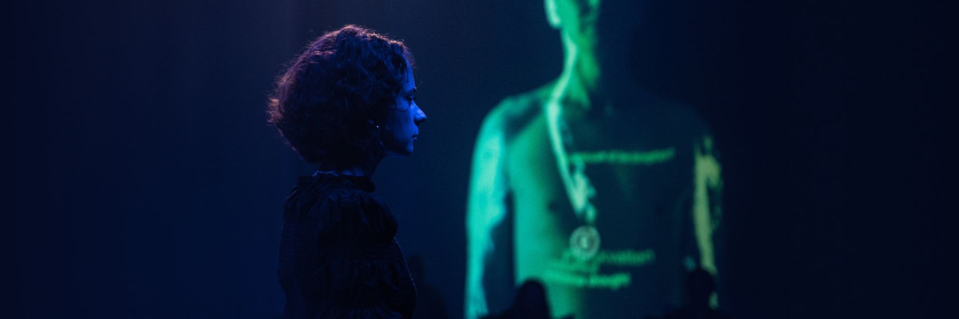 woman standing in front of a dark background with green video projection